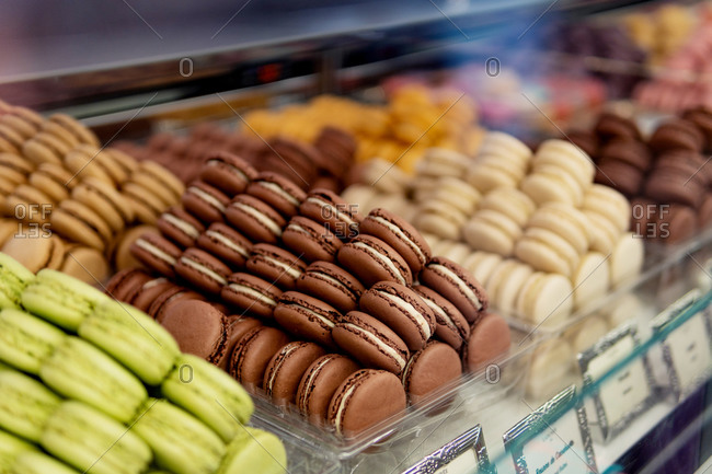 Many colorful tasty macaroons of different colors with various fillings and tastes assorting by colors into containers standing on show window in pastry shop