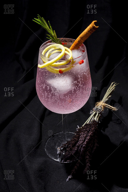 Gin tonic cocktail with pink tonic water, pink pepper, rosemary, mint, cinnamon, lemon and orange on dark background