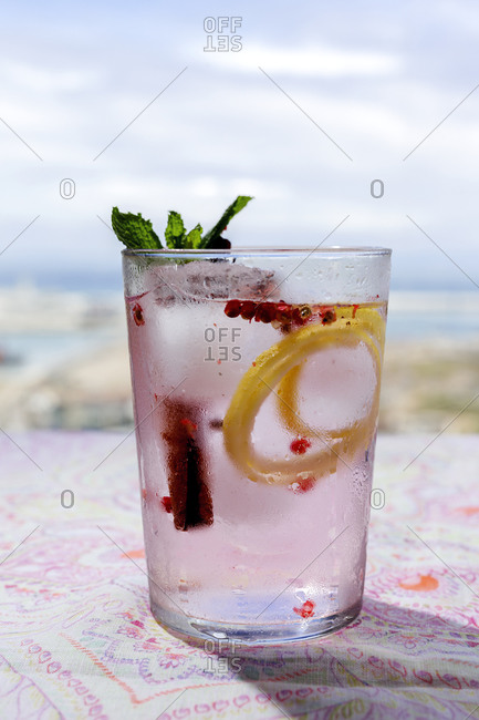 Gin tonic cocktail with pink tonic water, pink pepper, rosemary, mint, cinnamon, lemon and orange in the sunlight on a restaurant table