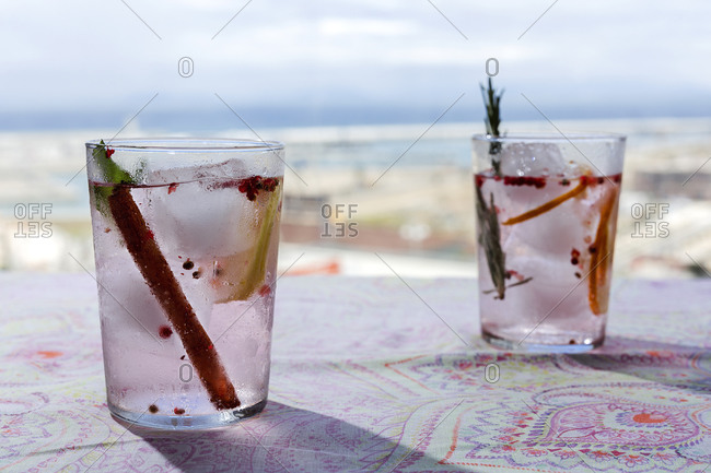 Gin tonic cocktail with pink tonic water, pink pepper, rosemary, mint, cinnamon, lemon and orange in the sunlight on a restaurant table