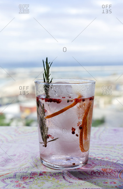 Gin tonic cocktail with pink tonic water, pink pepper, rosemary, mint, cinnamon, lemon and orange in the sunlight on a restaurant table