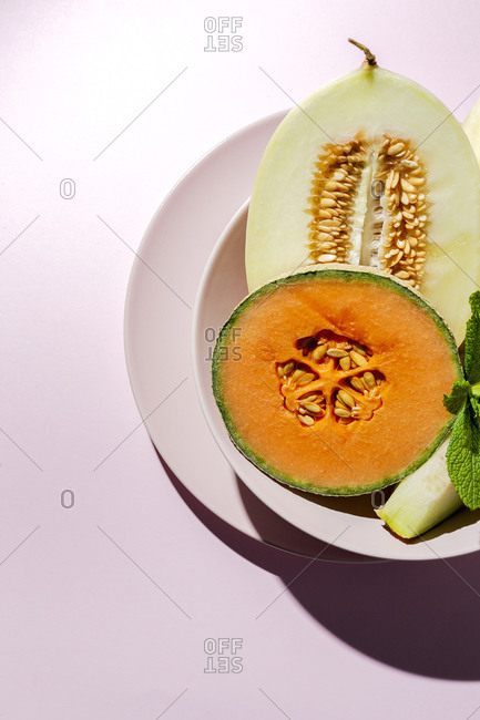Fresh assortment melon with mint  on pink background with high contrast light. Vegan food concept. Healthy food