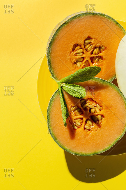 Fresh assortment melon with mint  on yellow background with high contrast light. Vegan food concept. Healthy food