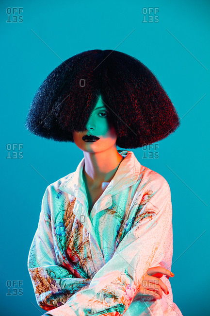 Attractive woman in oriental silk robe with floral ornament and lavish wig under colorful illumination