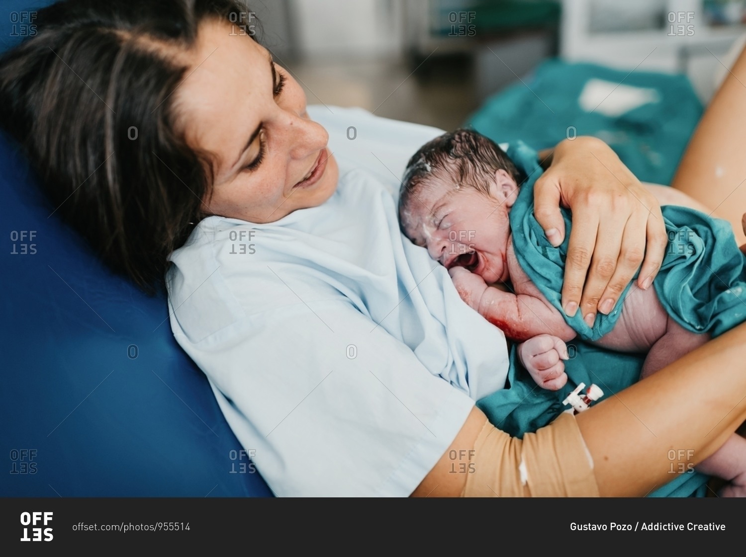 High angle of cheerful adult woman embracing newborn child covered with blood after giving birth in delivery room of contemporary hospital