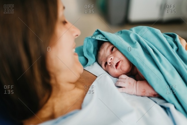 High angle of cheerful adult woman embracing newborn child covered with blood after giving birth in delivery room of contemporary hospital