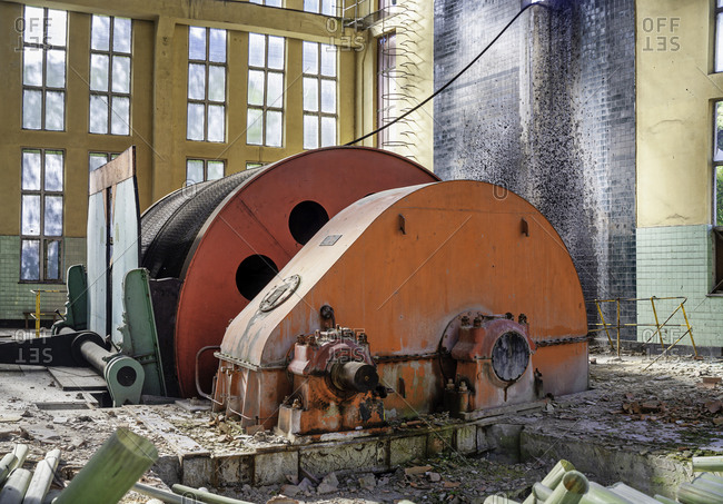 Industrial circular machine with metal mechanism locating inside deserted ownerless dilapidated industrial workshop with light walls and large arched windows