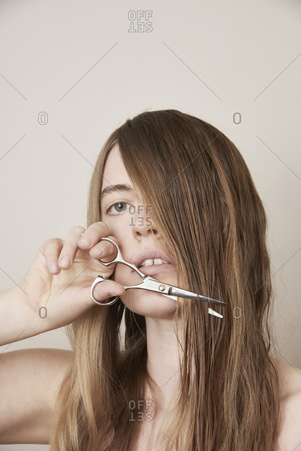 Young woman preparing to cut her long blond hair with scissors