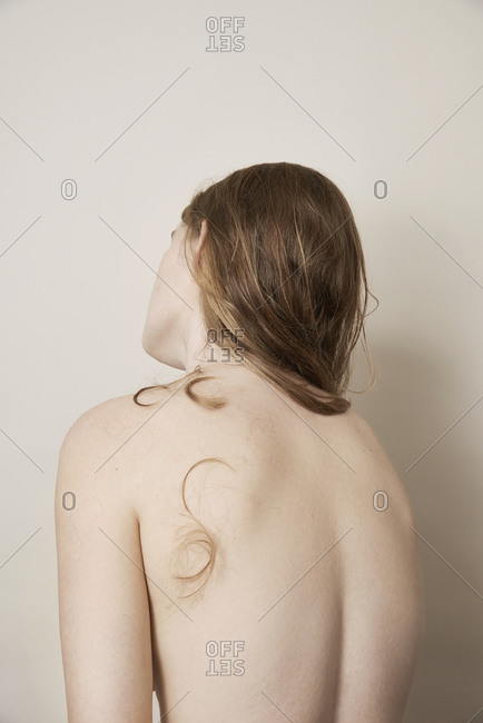 Rear view of young woman with long hair and cut strand on her nude backside