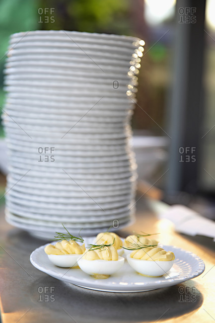 Deviled eggs with dill garnish beside a stack of plates