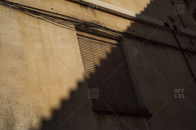 Sunlight and shadows on side of gray building with window and blinds