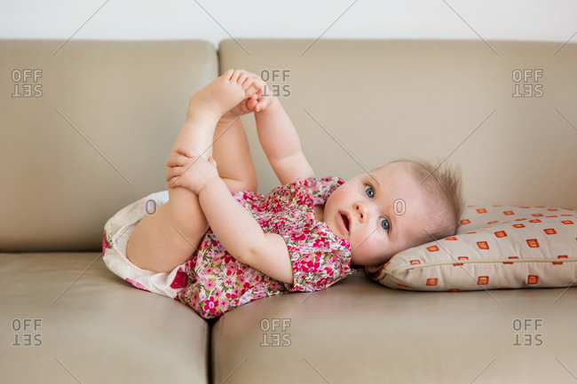 Cute baby girl lying on couch holding her feet