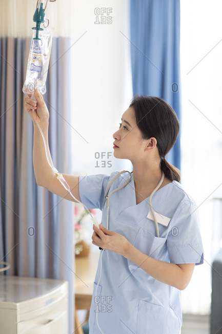 Young Chinese nurse checking IV drip in hospital ward