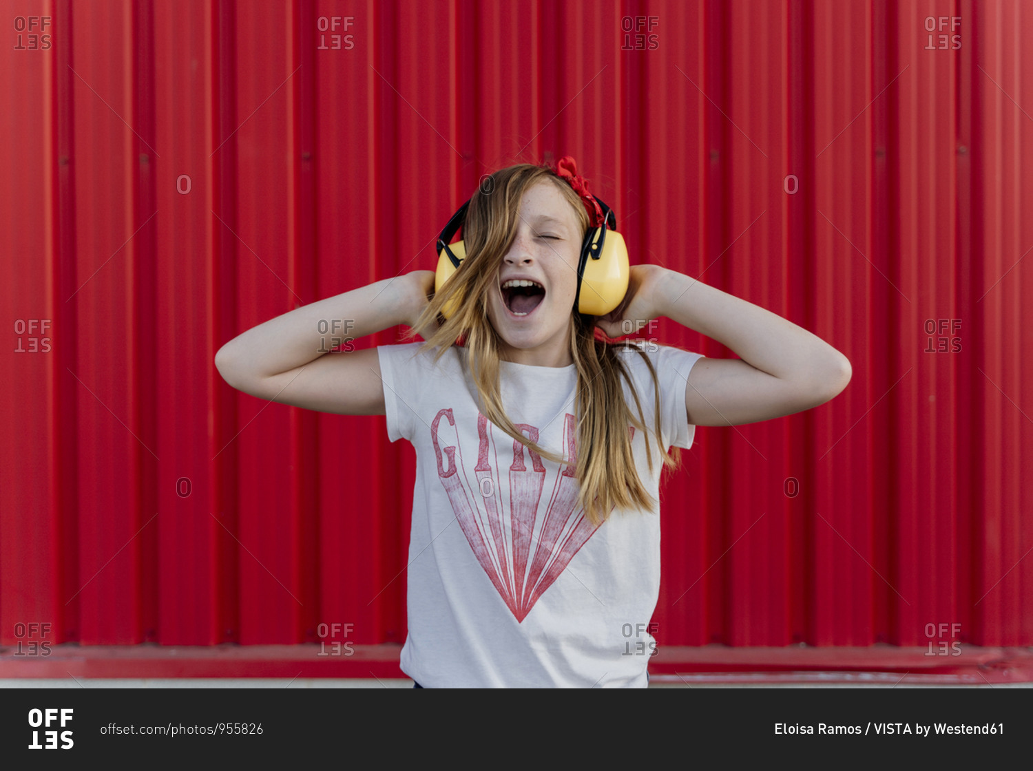 Girl with ear defenders in front of red wall