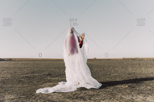 Young man standing in barren land trapped in a plastic foil