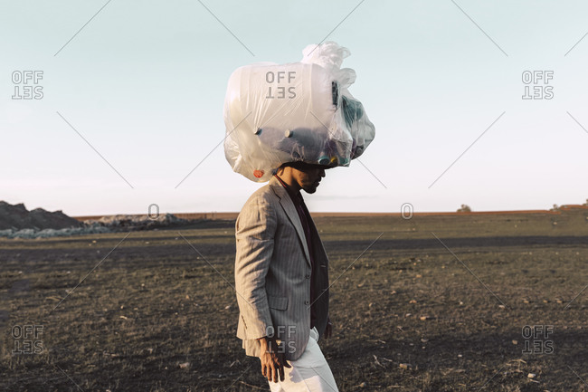 Young man carrying bag with plastic bottles on his head in barren land