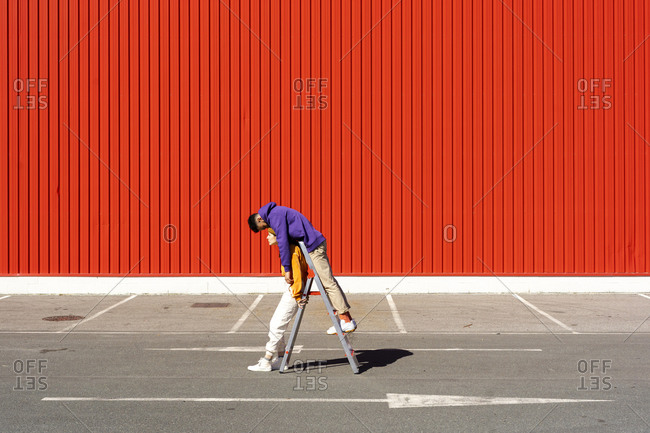 Young man and woman performing with a ladder in front of a red wall