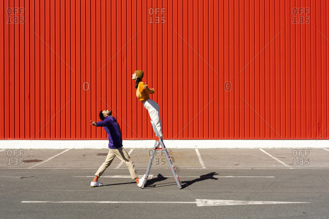Young man and woman performing with a ladder in front of a red wall