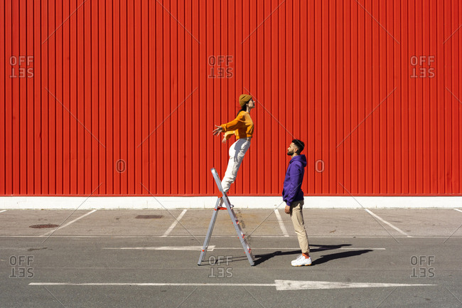 Young man and woman performing with a ladder in front of a red wall