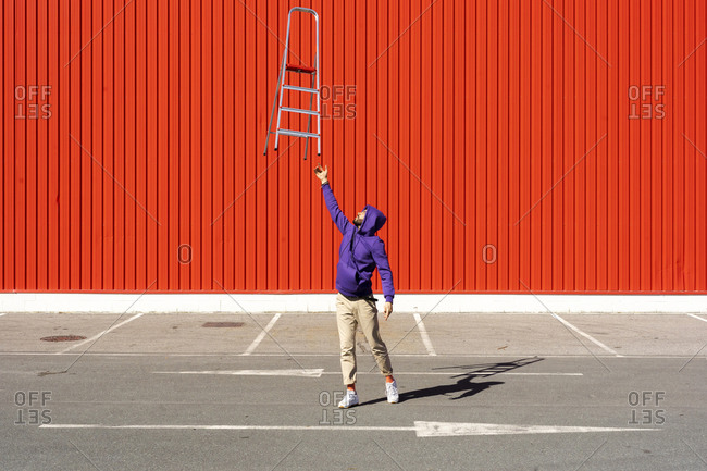 Young man balancing a ladder in front of a red wall