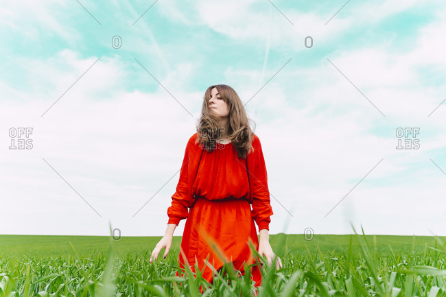 Woman wearing red dress relaxing in a field with eyes closed