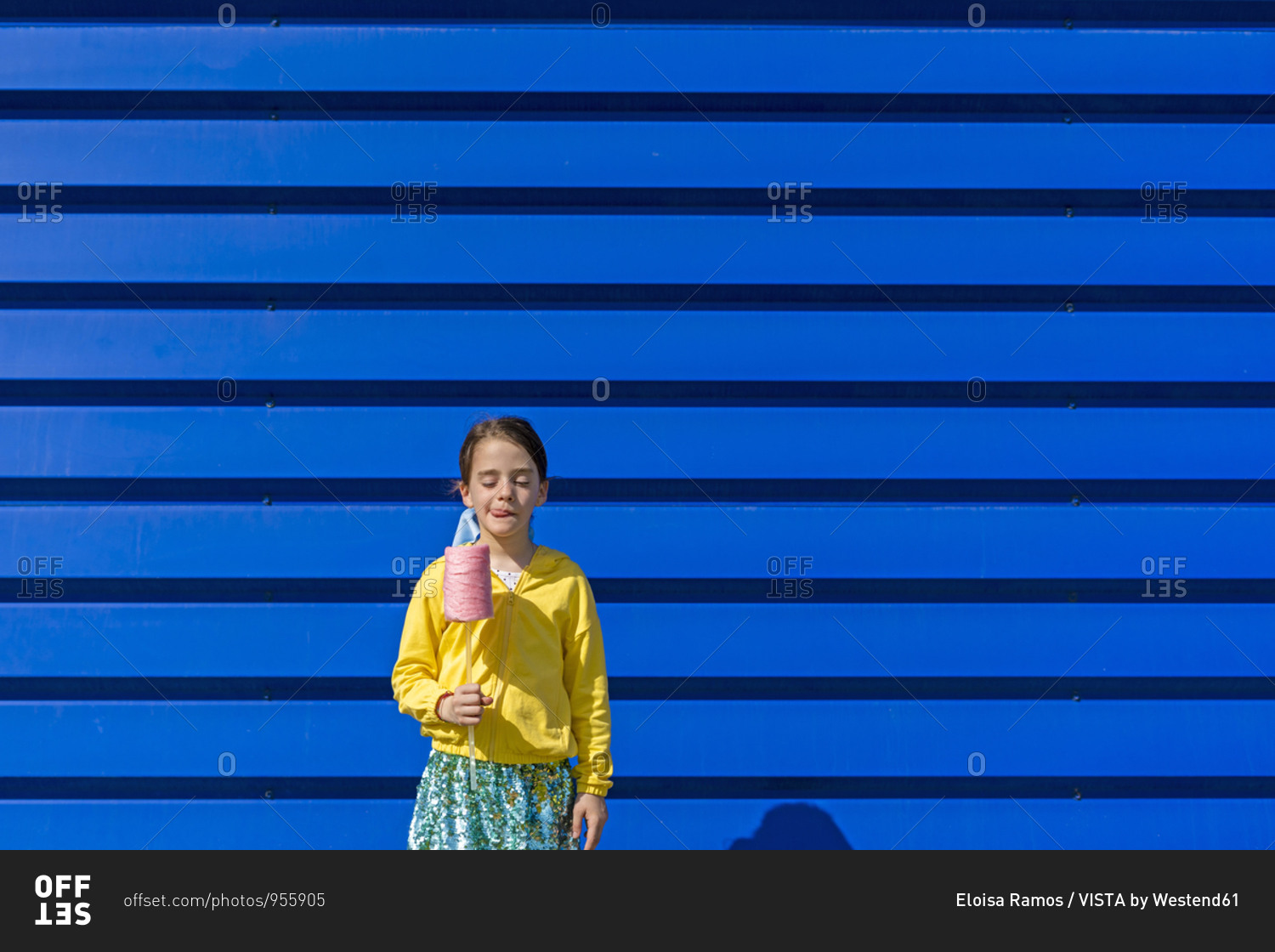 Little girl with fake ice cream standing in front of blue background licking lips