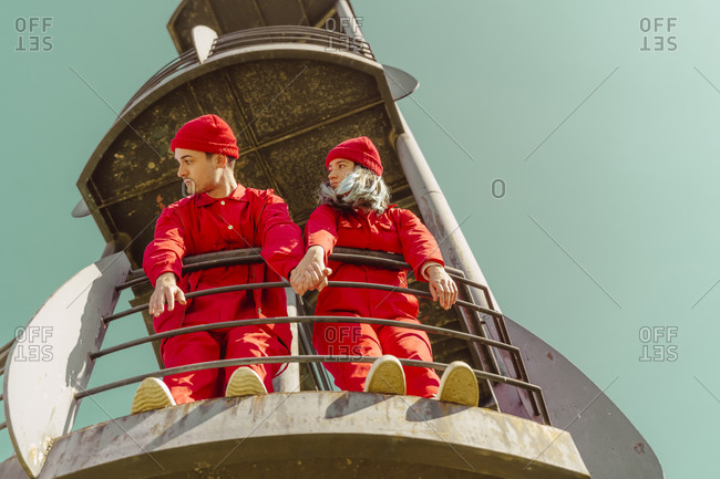 Young couple wearing red overalls and hats standing on platform looking at distance