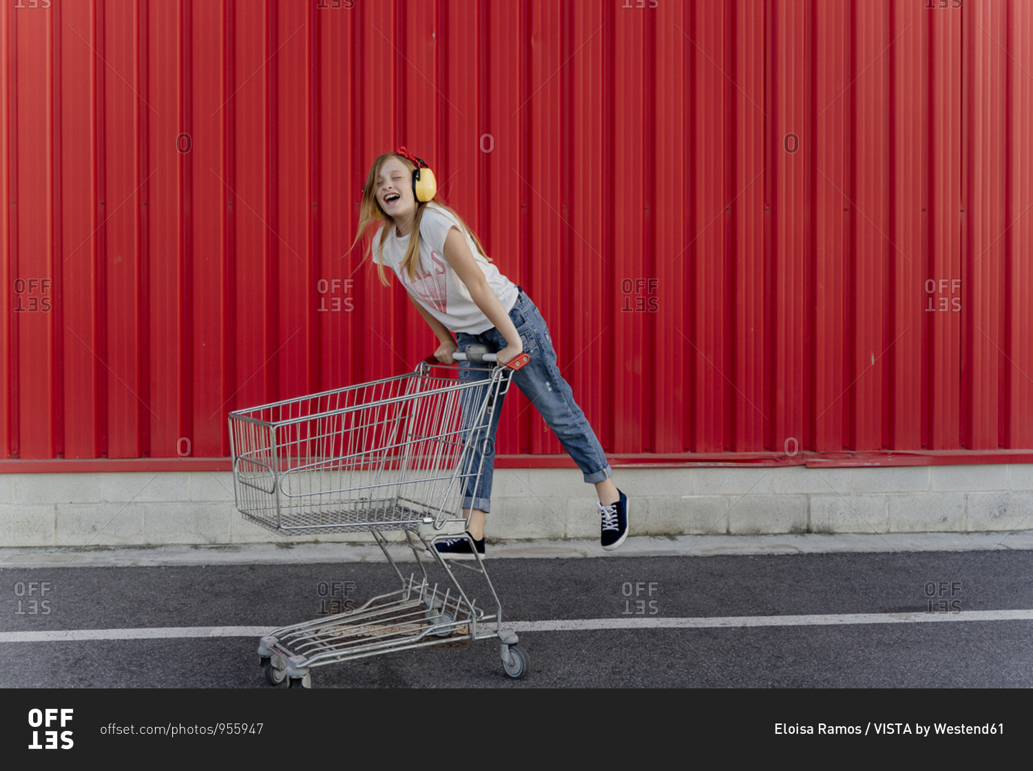Girl with a shopping cart and ear defender in front of red wall
