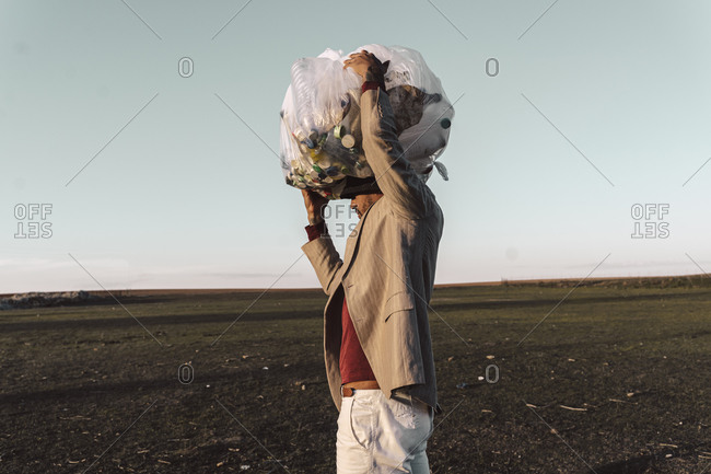 Young man carrying bag with plastic bottles on his head in barren land