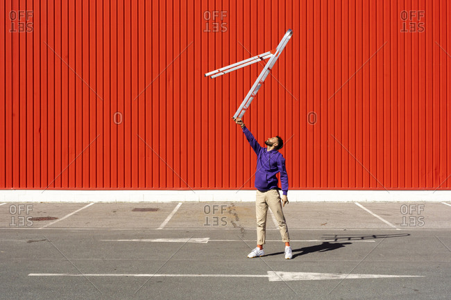Young man balancing a ladder in front of a red wall