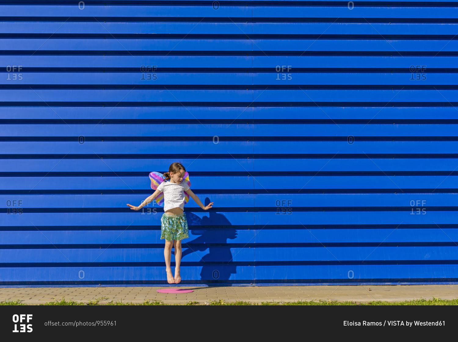 Little girl with colorful butterfly wings jumping in the air in front of blue background