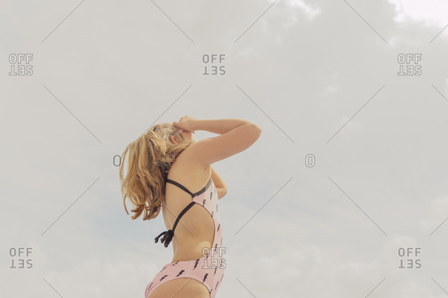 Blond girl wearing pink swimsuit standing against cloudy sky