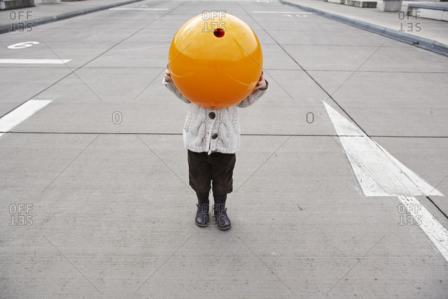 Little girl standing in street- hiding under orange sphere