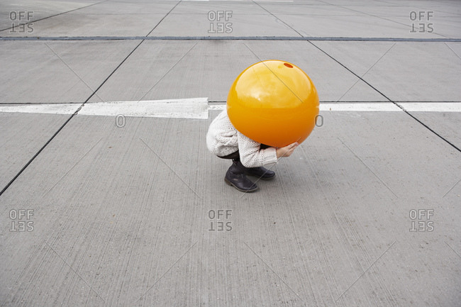 Little girl crouching in street- hiding under orange sphere