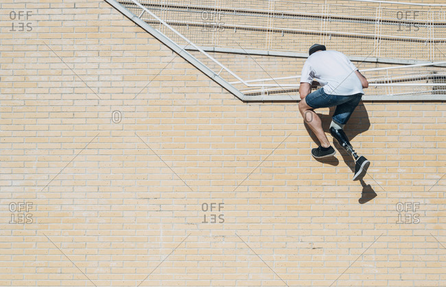 Young man with leg prosthesis climbing up brick wall