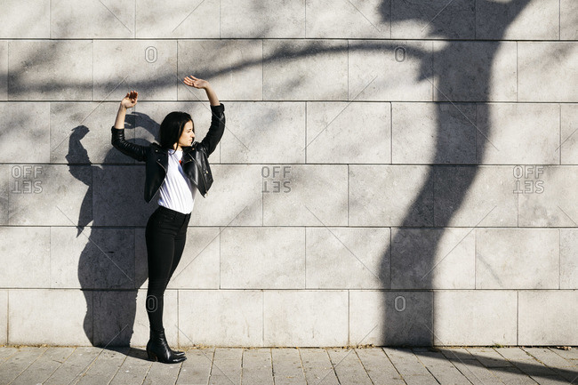 Young woman making shadows on a white wall with a shadow of a tree