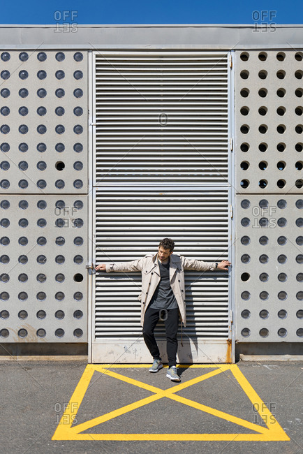 Mid adult man standing in yellow marked area in front of concrete wall- with arms outstretched