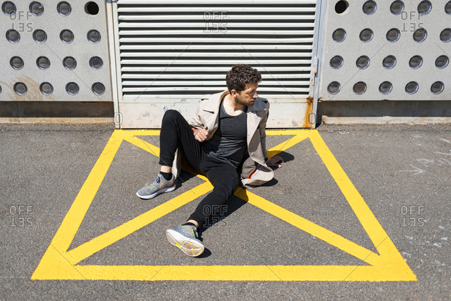 Helpless man sitting on ground in yellow marked area in front of concrete wall