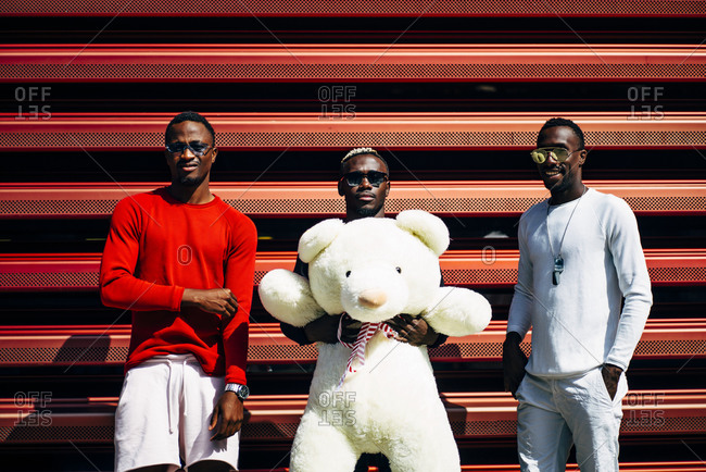 Portrait of three cool young men with huge teddy bear at red wall