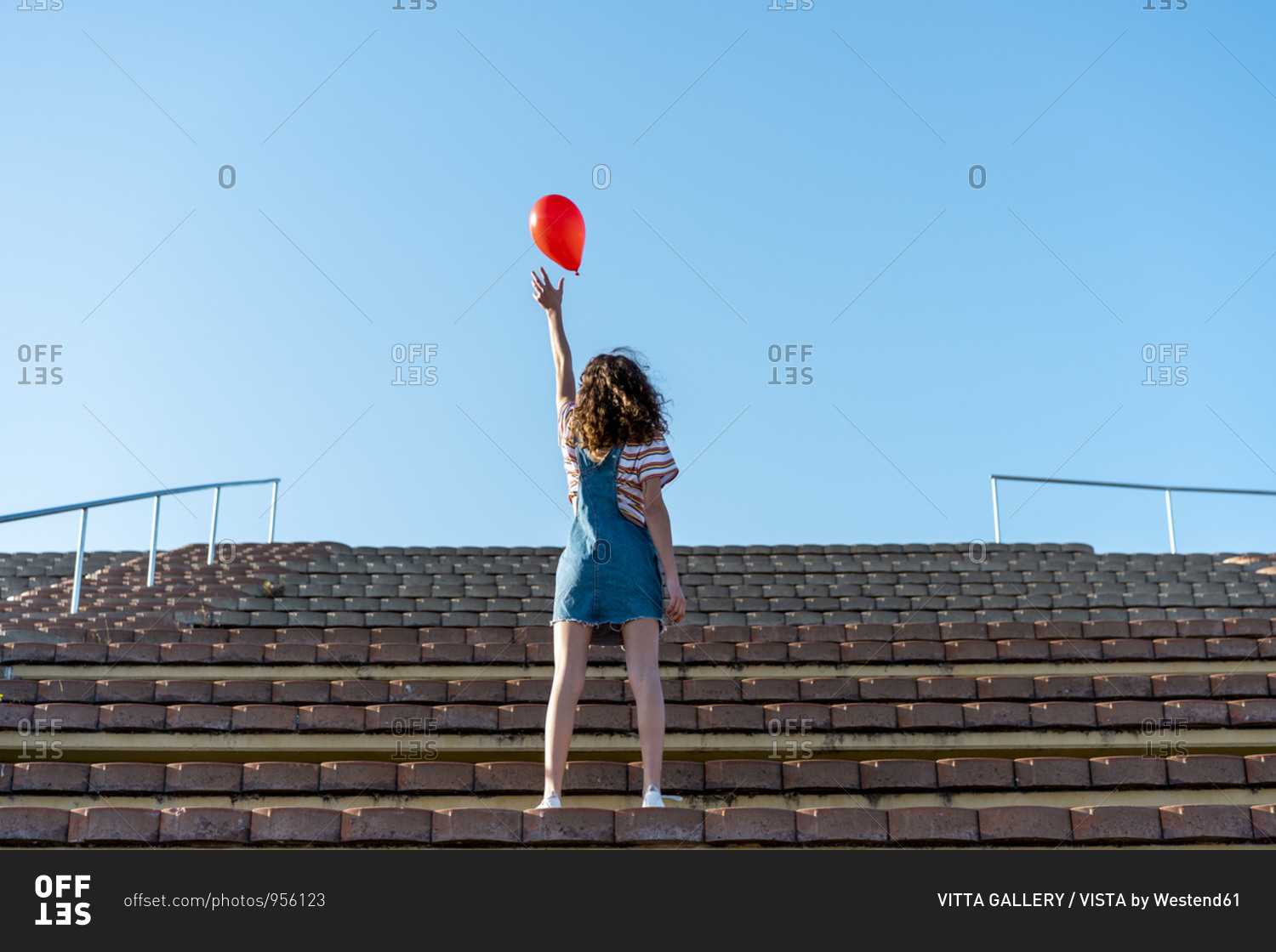 Young woman standing on grandstand- letting go of a red balloon