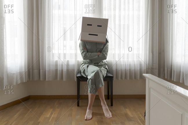 Woman wearing a card box on head with bored smiley sitting on chair with crossed arms