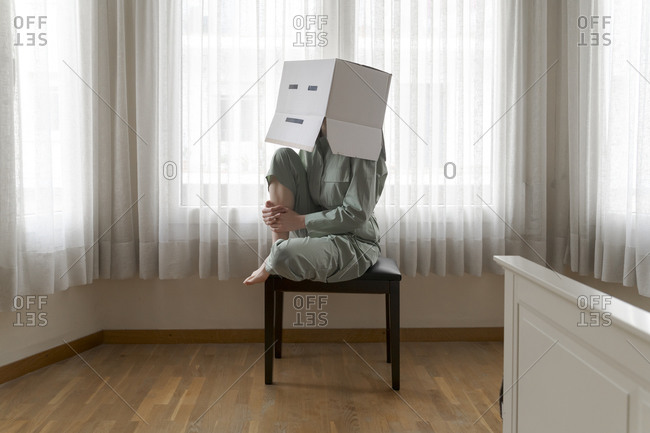 Woman wearing a card box on head with bored smiley sitting on chair
