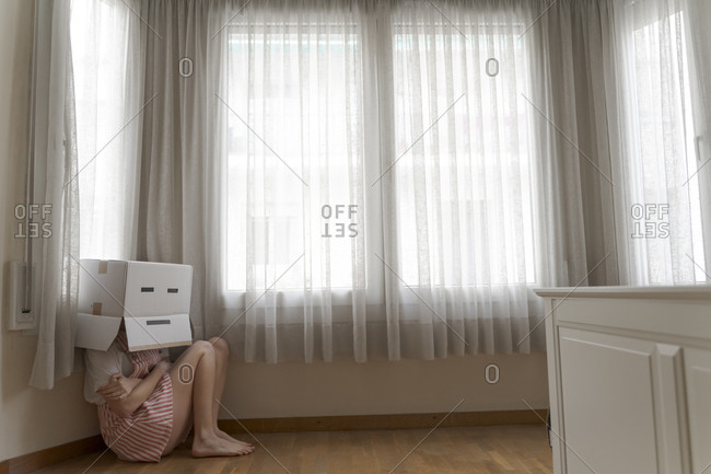 Woman wearing a card box on head with bored smiley and cowering on the floor