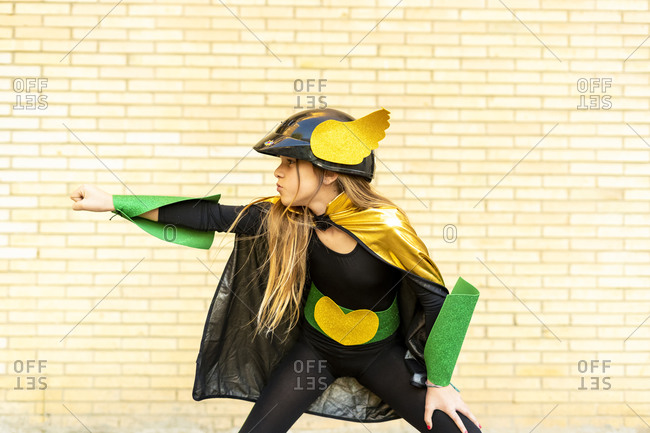 Girl in super heroine costume posing at brick wall