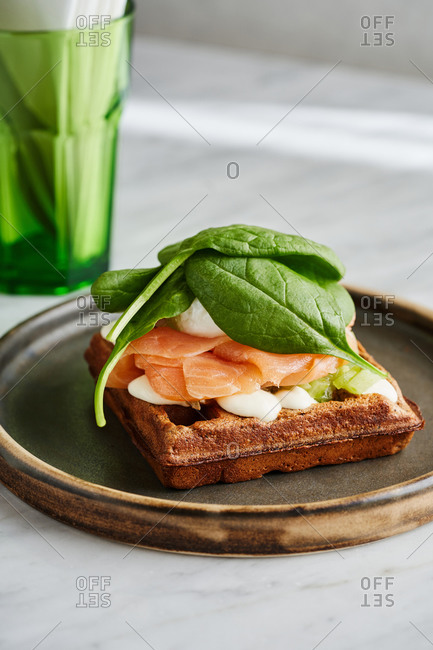 Beautifully plated savory breakfast dish - waffle topped with creme fraiche, salmon gravlax, poached egg and baby spinach leaves