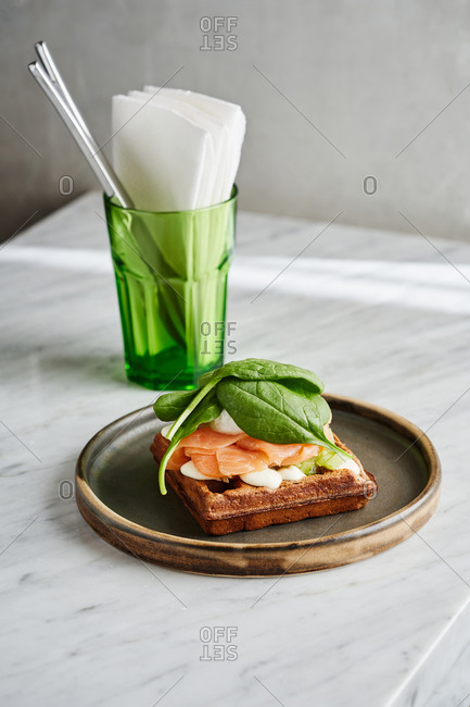Crispy savory waffle topped with slices of smoked salmon, bechamel sauce, poached egg and baby spinach