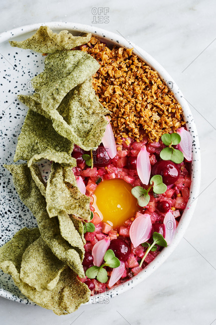 Close up top angle view of beautifully plated tartar dish with egg yolk, puffed rice and bread crumble