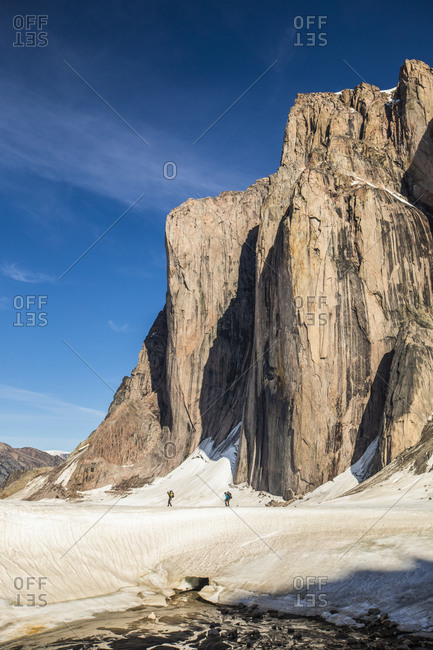 Distant view of two mountaineers hiking under large mountain cliff.