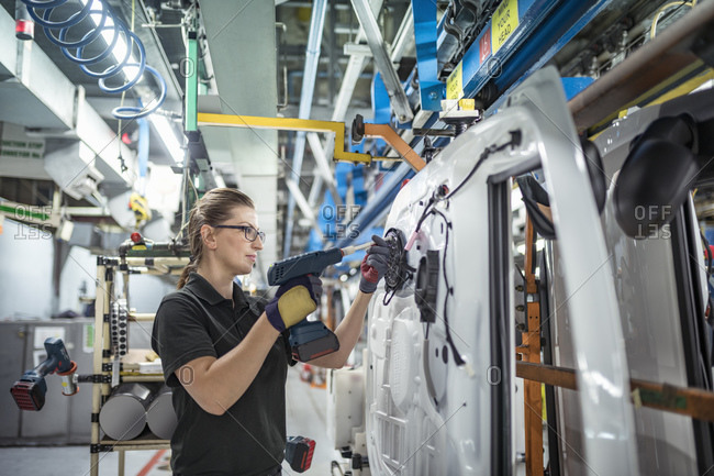 Female worker assembling car doors on production line in a car factory