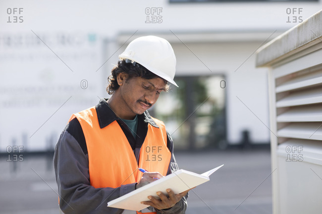 Male engineer outside industrial building writing in notebook